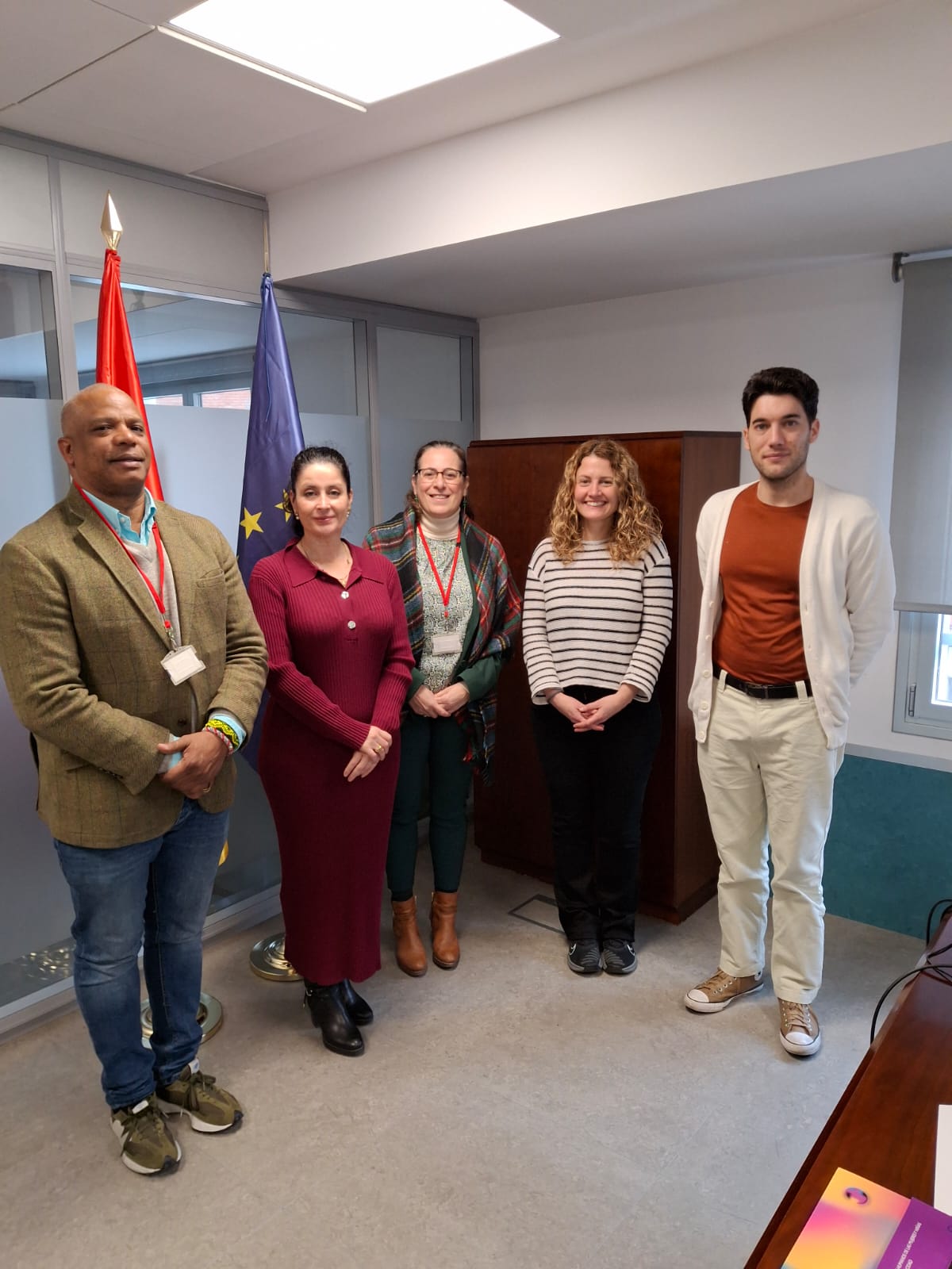 Grupo de cinco personas integrado por el equipo de la AINODI y de Afrohispanos, que están de pie mirando a la cámara. Tienen detrás a la izquierda las bandera de España y de la UE