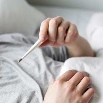 Manos y parte del torso de una persona en la cama sosteniendo un termómetro digital