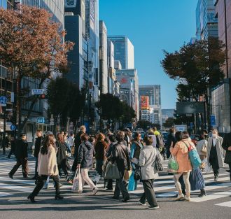 Multitud de personas atravesando un paso de peatones de una gran ciudad con numerosos edificios altos y modernos