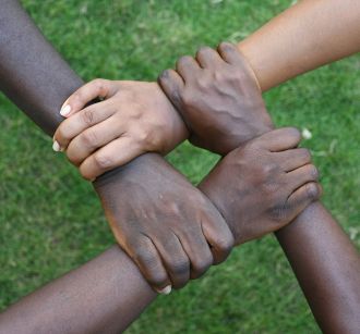 Cuatro manos entrelazadas de personas negras cogiéndose las muñecas